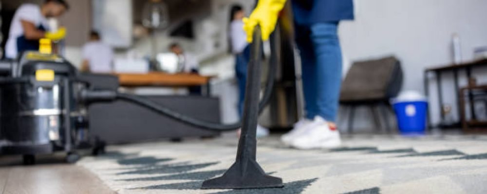 Close-up on a professional cleaner vacuuming a carpet while working at an apartment - housework concepts